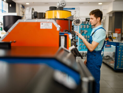 Plumber choosing boiler with furnace, plumbering Plumber in uniform choosing boiler with furnace at showcase in plumbering store. Man with notebook buying sanitary engineering in shop, water heater choice